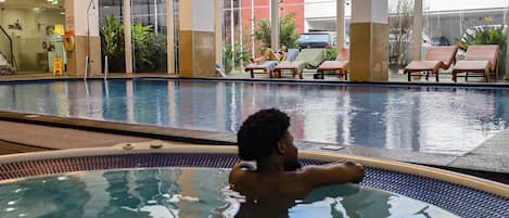 An indoor swimming pool with lounge chairs and a person relaxing in the water.