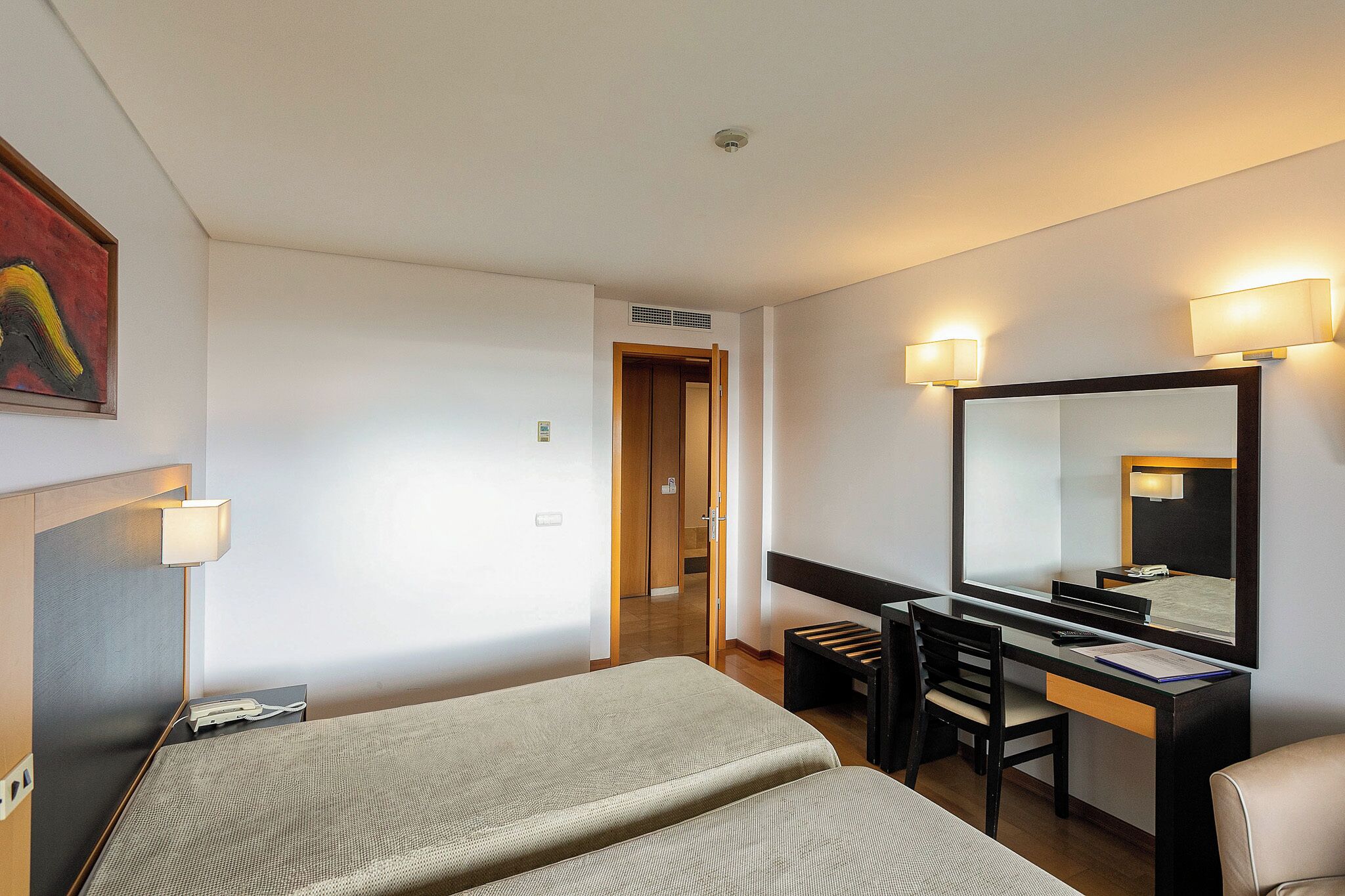 Habitación de hotel con cama, escritorio, silla y un espejo grande.