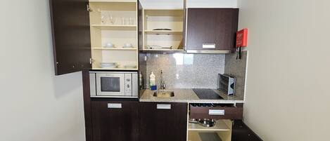 Een kleine keuken met een magnetron, spoelbak en opbergkasten.