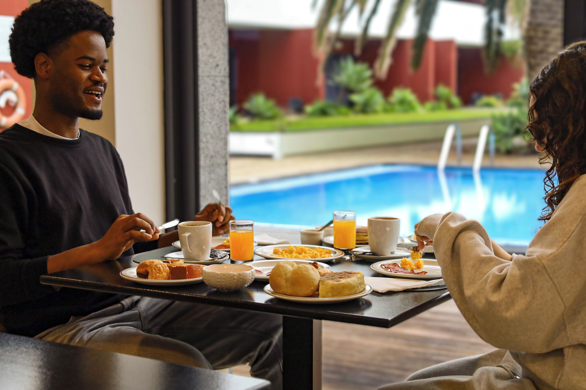 Comedor con vista a la piscina, con platos de desayuno, jugo de naranja y un ambiente relajado.
