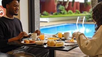 Comedor con vista a la piscina, con platos de desayuno, jugo de naranja y un ambiente relajado.