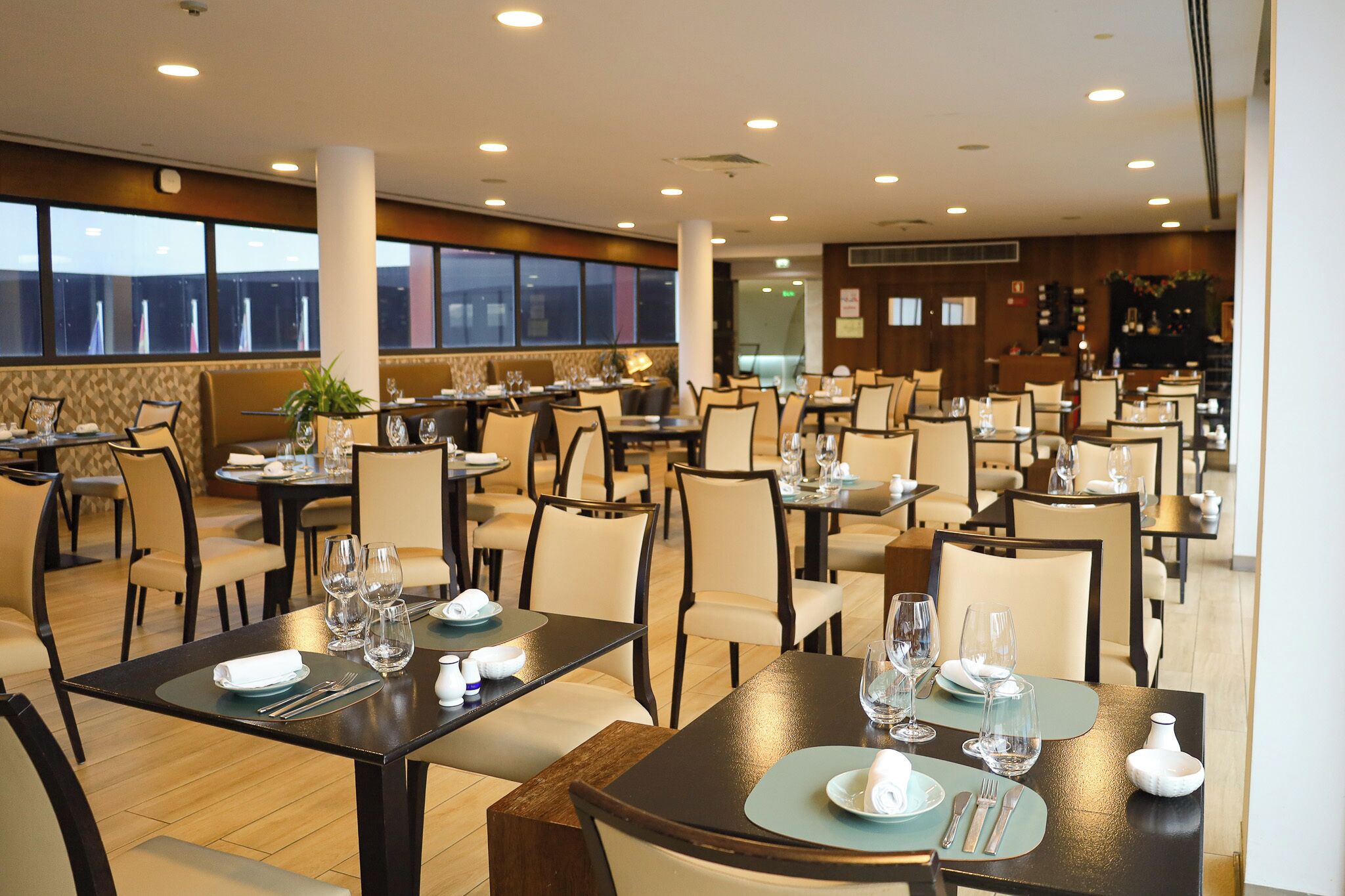 Um restaurante espaçoso com várias mesas e cadeiras, grandes janelas e um design de interiores moderno.