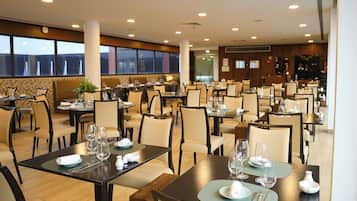 Um restaurante espaçoso com várias mesas e cadeiras, grandes janelas e um design de interiores moderno.
