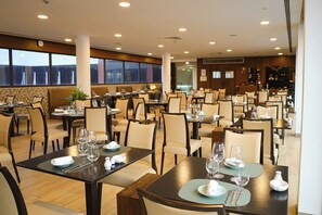 A spacious restaurant with multiple tables and chairs, large windows, and a modern interior design.