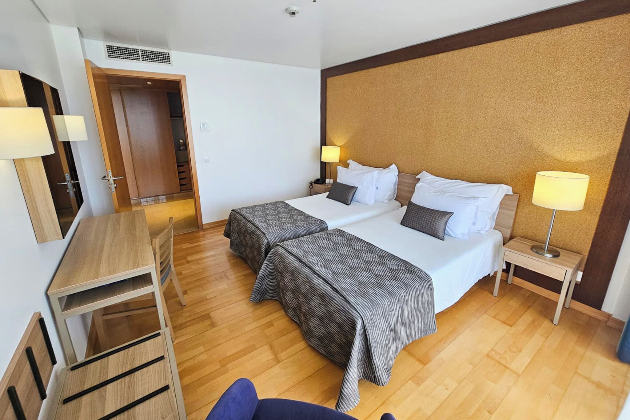 A hotel room with a bed, bedside tables, a desk, and a chair.