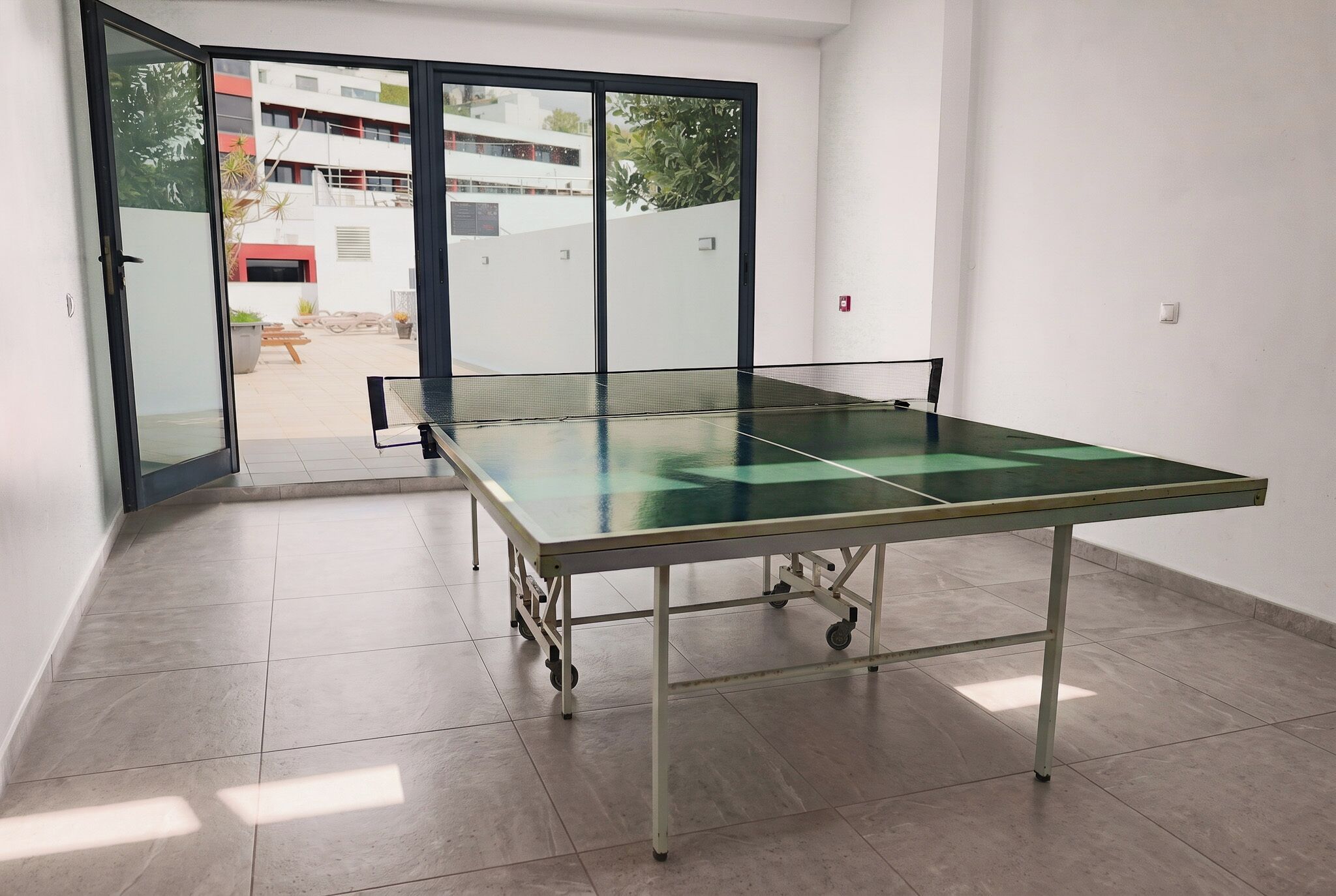 Um quarto com mesa de pingue-pongue, porta de vidro deslizante para o exterior e piso revestido de azulejos.