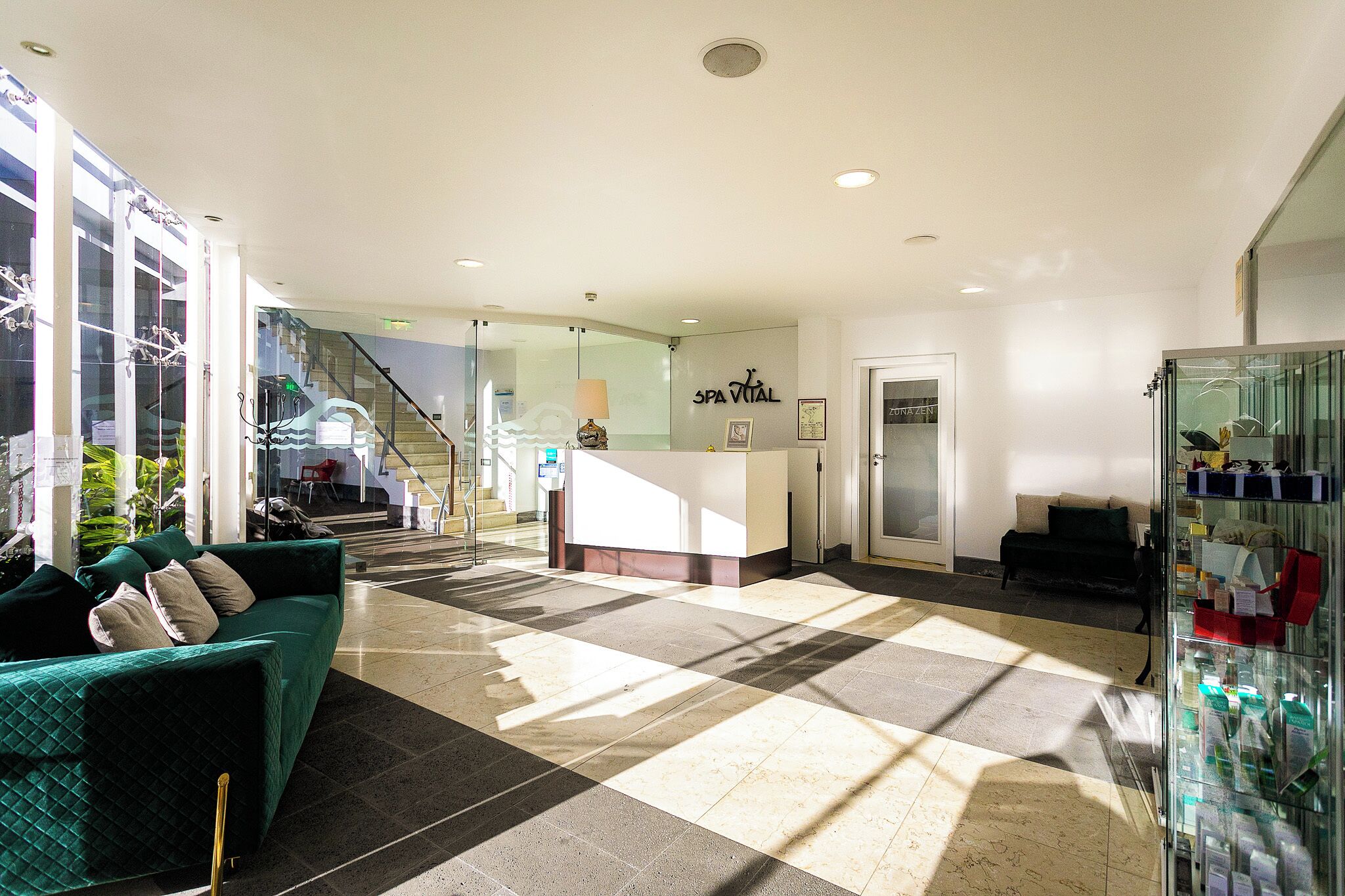 Un vestíbulo de hotel con un mostrador de recepción, una escalera y un sofá verde.