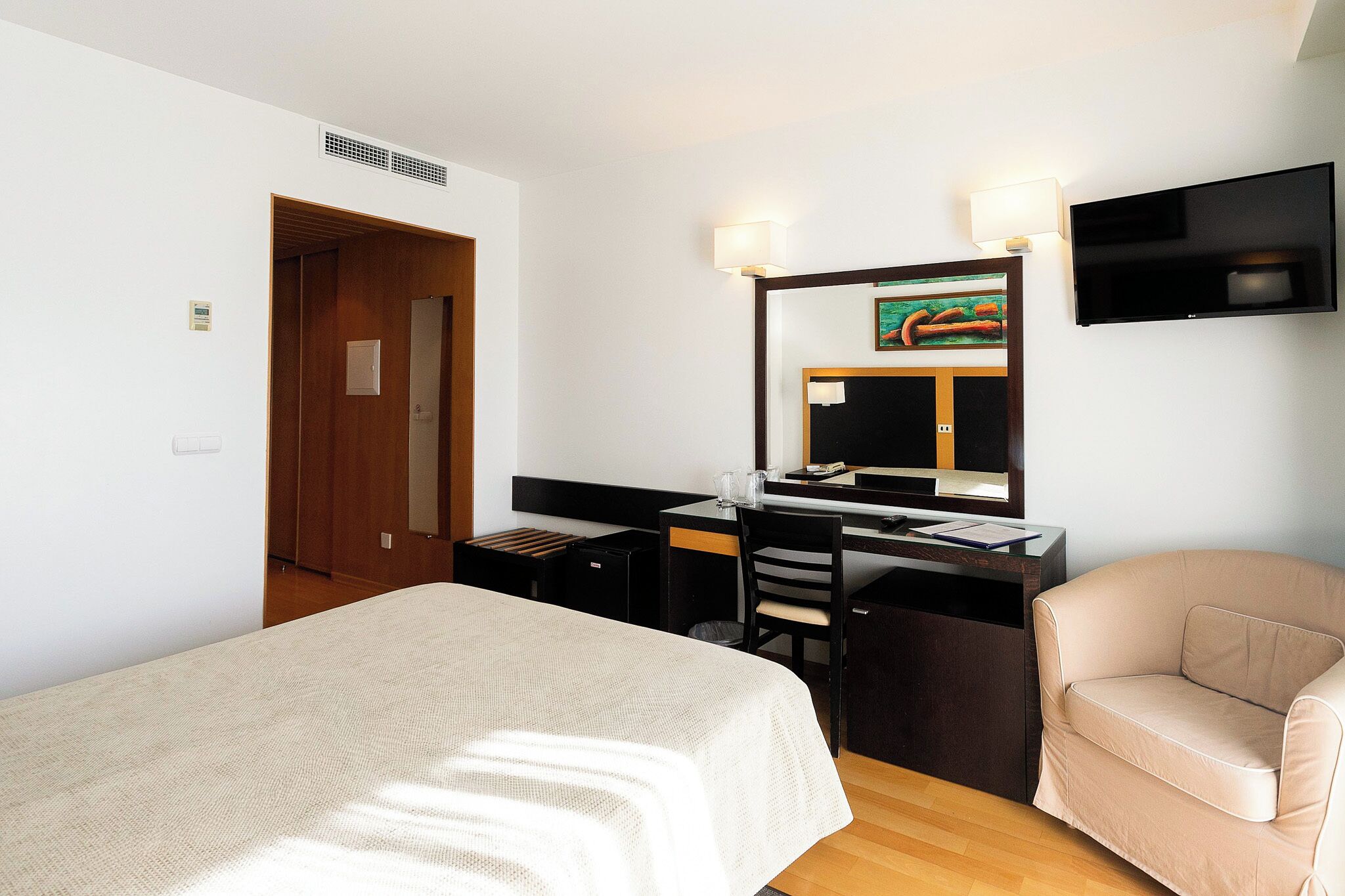 Una camera d'albergo con un letto, una scrivania, una sedia e un televisore fissato al muro.