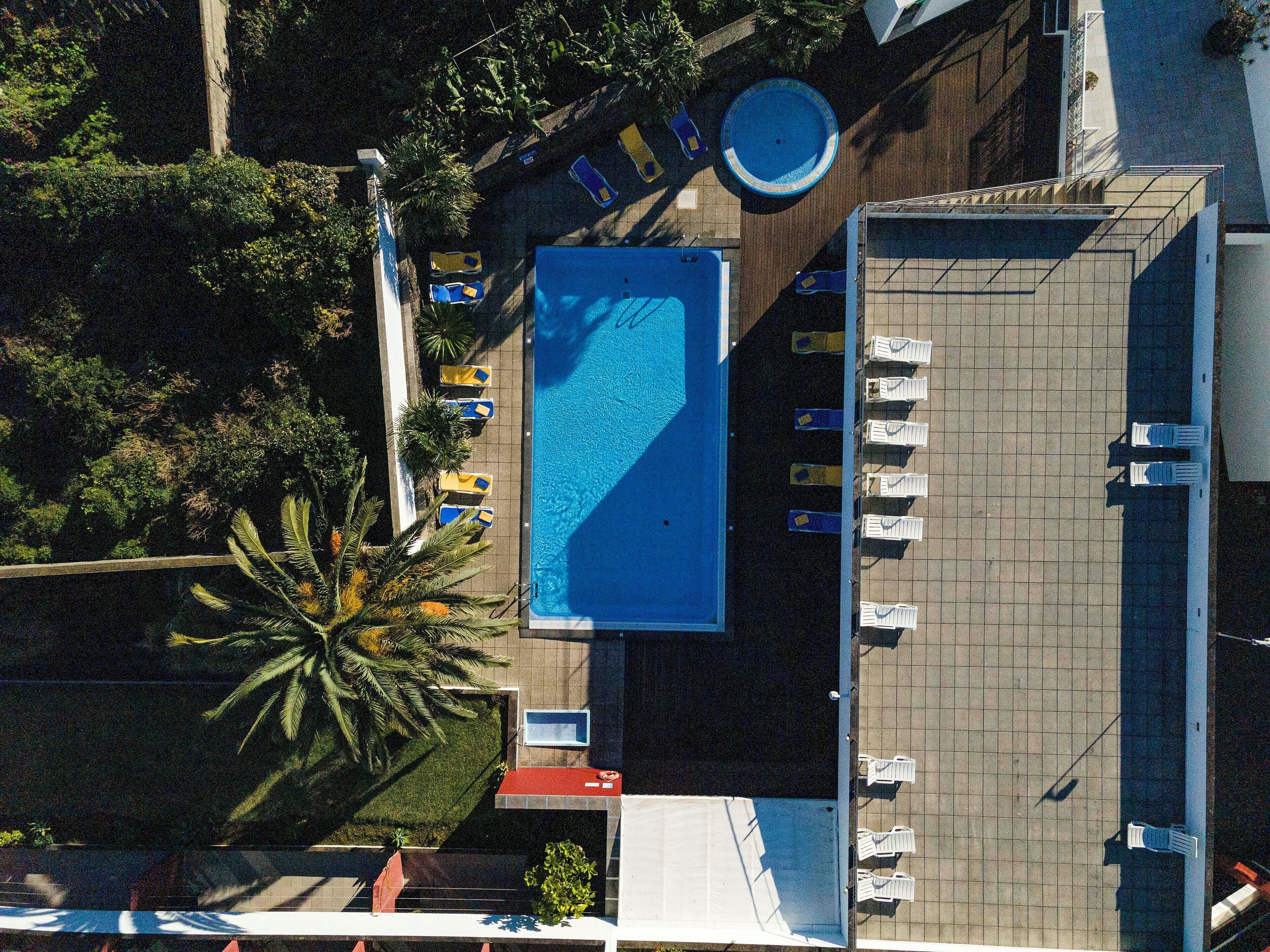 An aerial view of a hotel with a swimming pool, sun loungers, and a parking area.