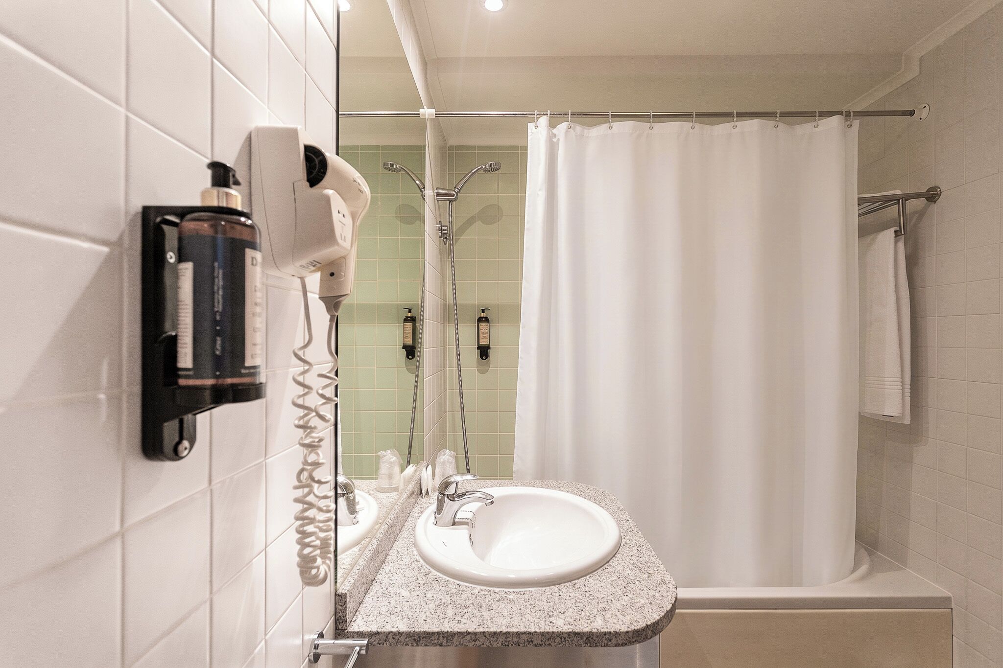 Un baño con un lavamanos blanco, ducha y un perchero para toallas.