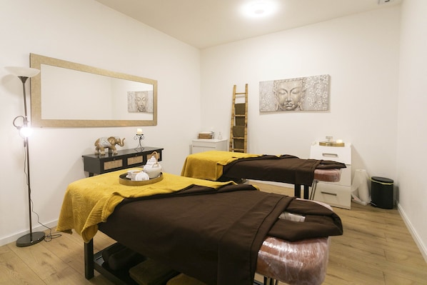 Ein Raum mit zwei Massagetischen, einer Stehlampe und Bildern an den Wänden.