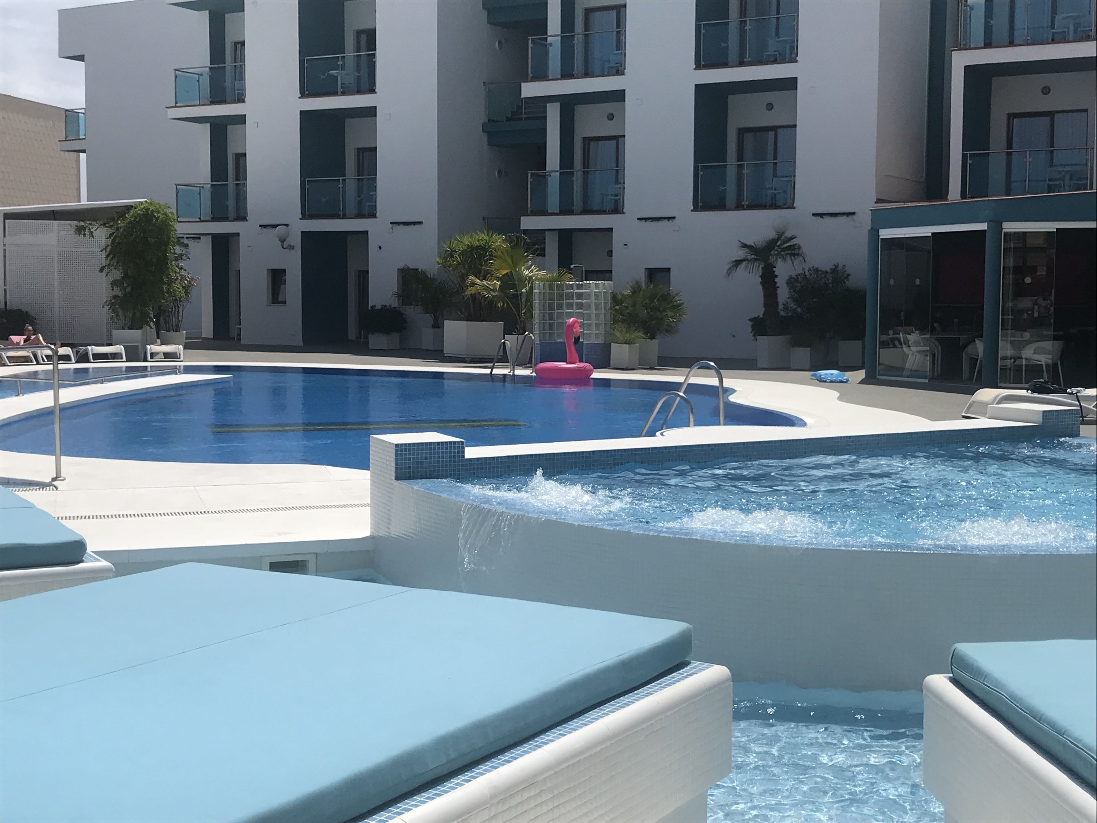 Une piscine avec une fontaine, des chaises longues et un bâtiment doté de balcons en arrière-plan.