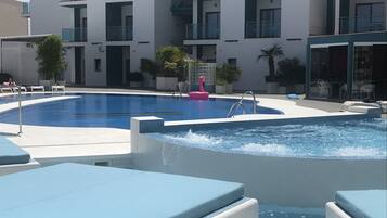 Une piscine avec une fontaine, des chaises longues et un bâtiment doté de balcons en arrière-plan.