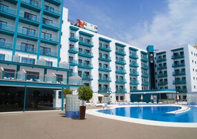 Een hotel met meerdere balkons, een zwembad en een heldere lucht.