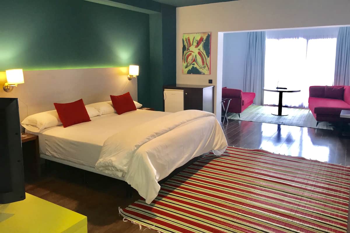 Une chambre d’hôtel avec un grand lit, un canapé rouge, une petite table et un tableau au mur.