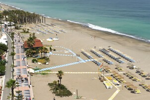 Een hotel aan het strand met een lange promenade, strandparasols en ligbedden.