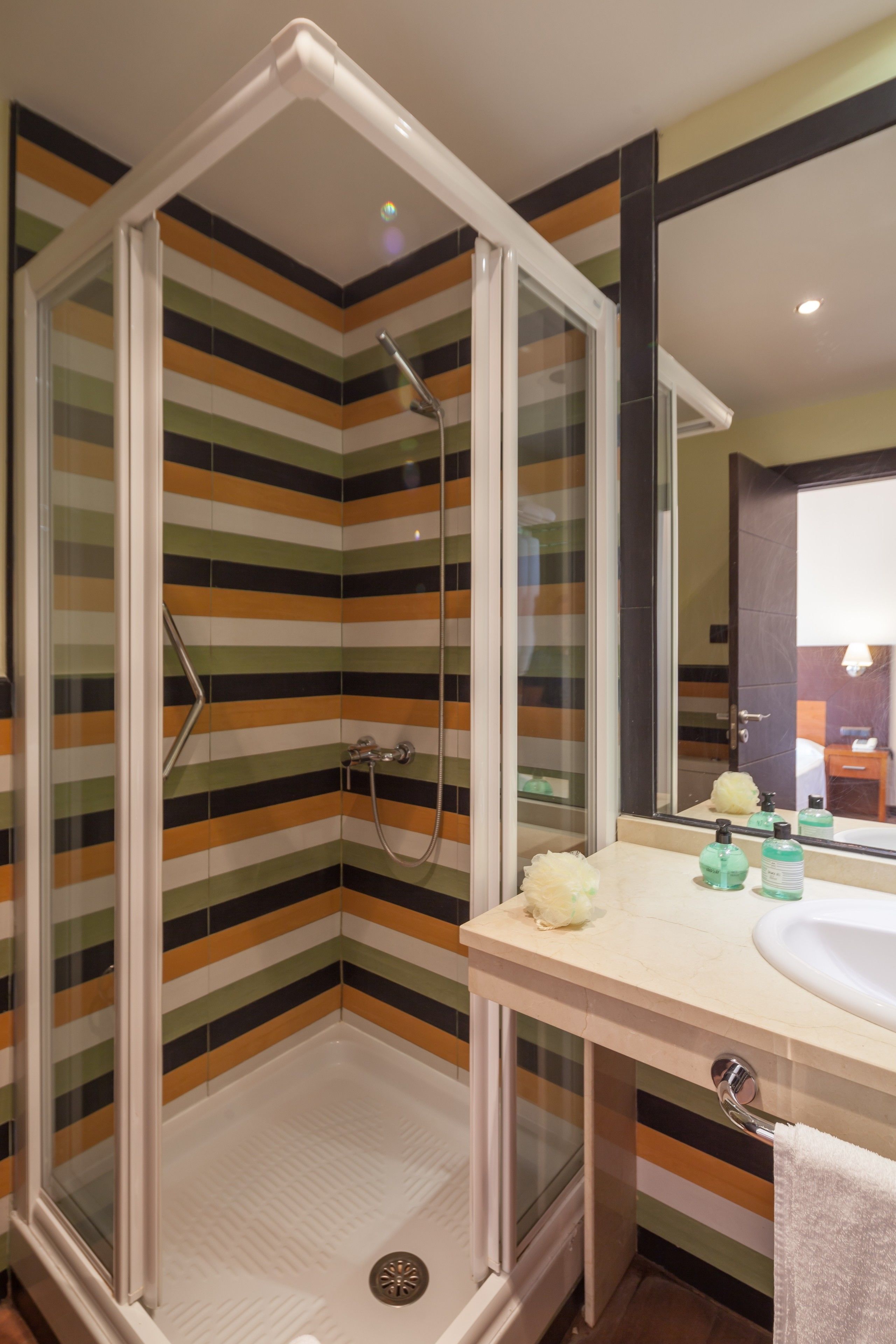 Un baño moderno con ducha de vidrio, paredes de azulejos a rayas, un lavabo con artículos de aseo personal y un espejo.