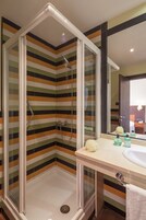 Een moderne badkamer met een douchecabine van glas, gestreepte wandtegels, een wastafel met toiletartikelen en een spiegel.