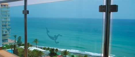 Un balcón con vista al océano y a una playa con sombrillas y palmeras.
