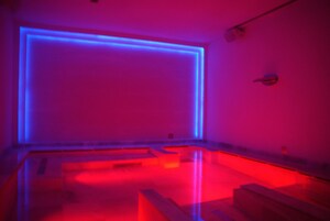 Um quarto com uma janela grande, uma televisão de tela plana e um banco de madeira.