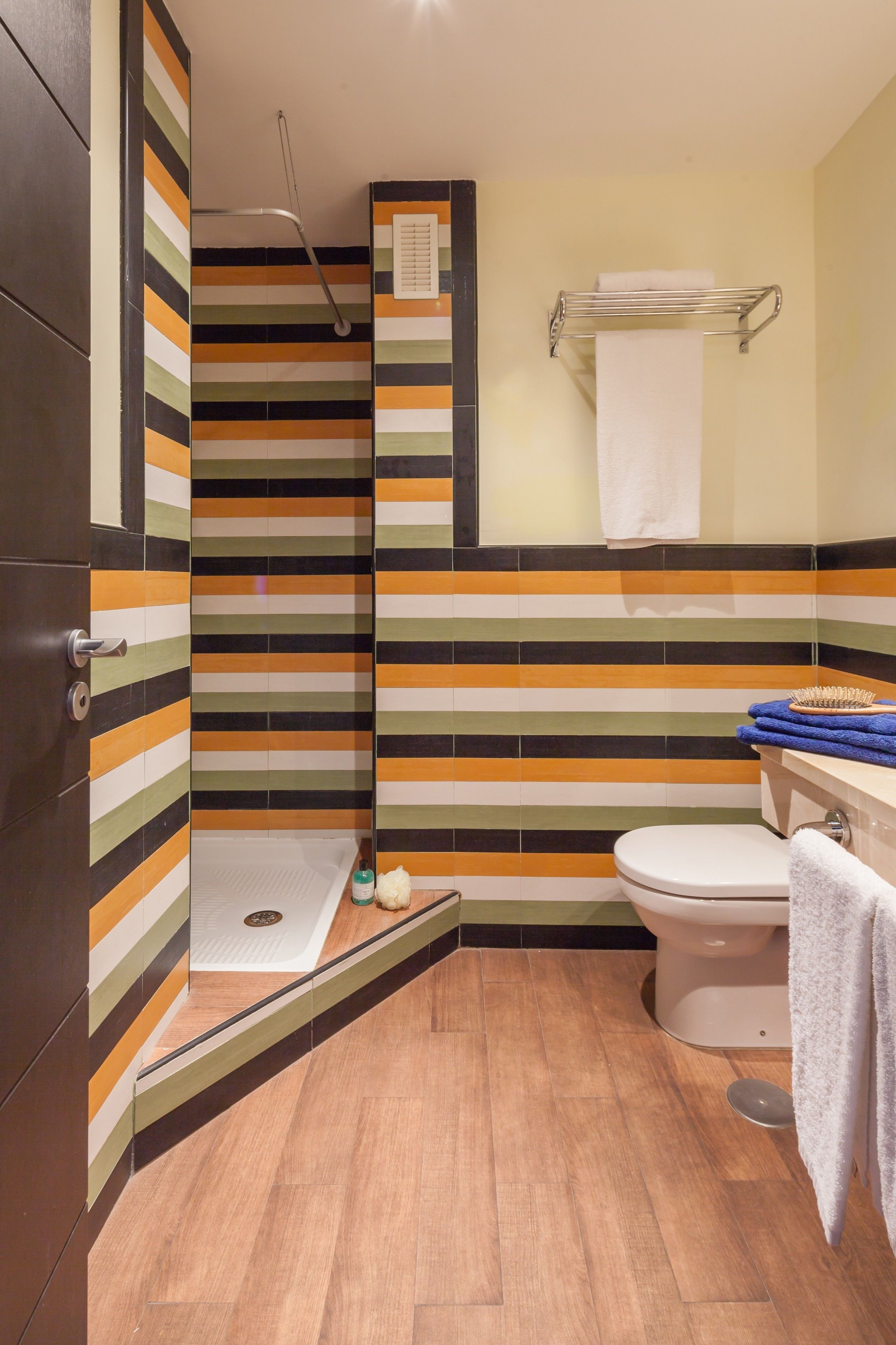 A bathroom with striped tile walls, a toilet, a shower, and a towel rack.
