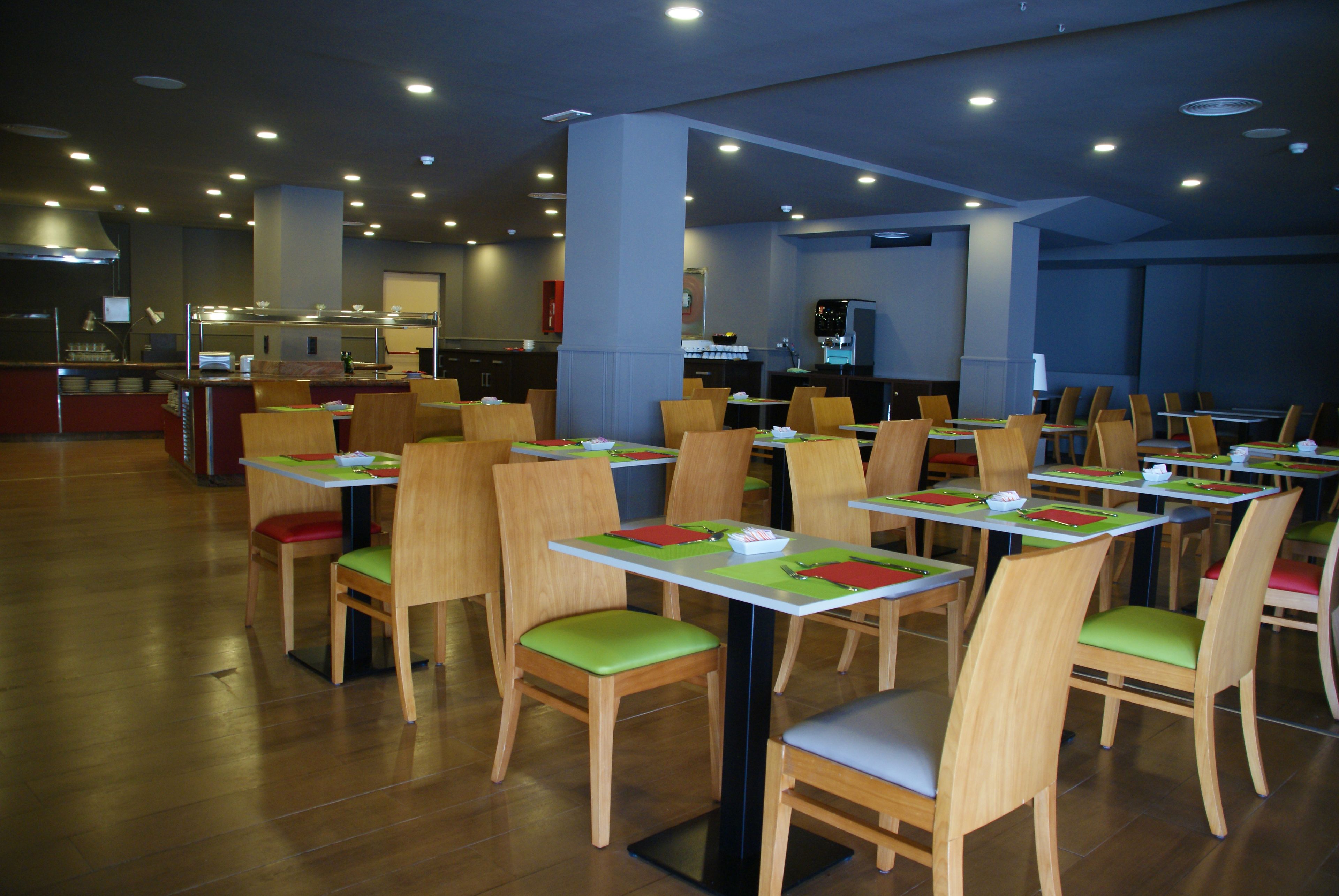A restaurant with multiple tables and chairs, a kitchen area in the background, and a clean, modern interior.