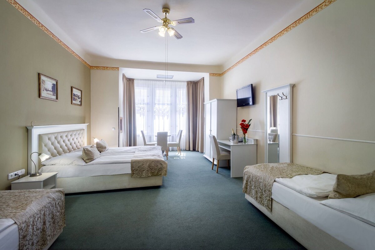 Ein Hotelzimmer mit zwei Betten, einem Schreibtisch, einem Fernseher und einem Deckenventilator.