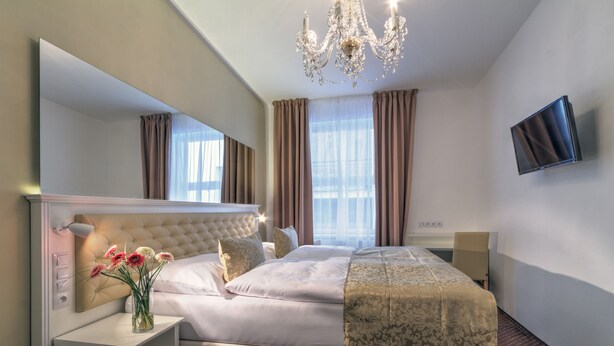 A hotel room with a large bed, a chandelier, a TV, and a window with curtains. - Hotel Taurus (Prague)