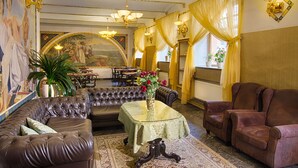A luxurious room with a large sofa, a smaller sofa, a table with a vase of flowers, and a mural on the wall. - Hotel Taurus (Prague)
