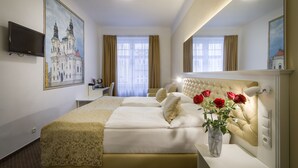 A hotel room with a large bed, a desk, a TV, and a painting of a cathedral.