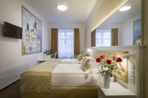 A hotel room with a large bed, a desk, a TV, and a painting of a cathedral.