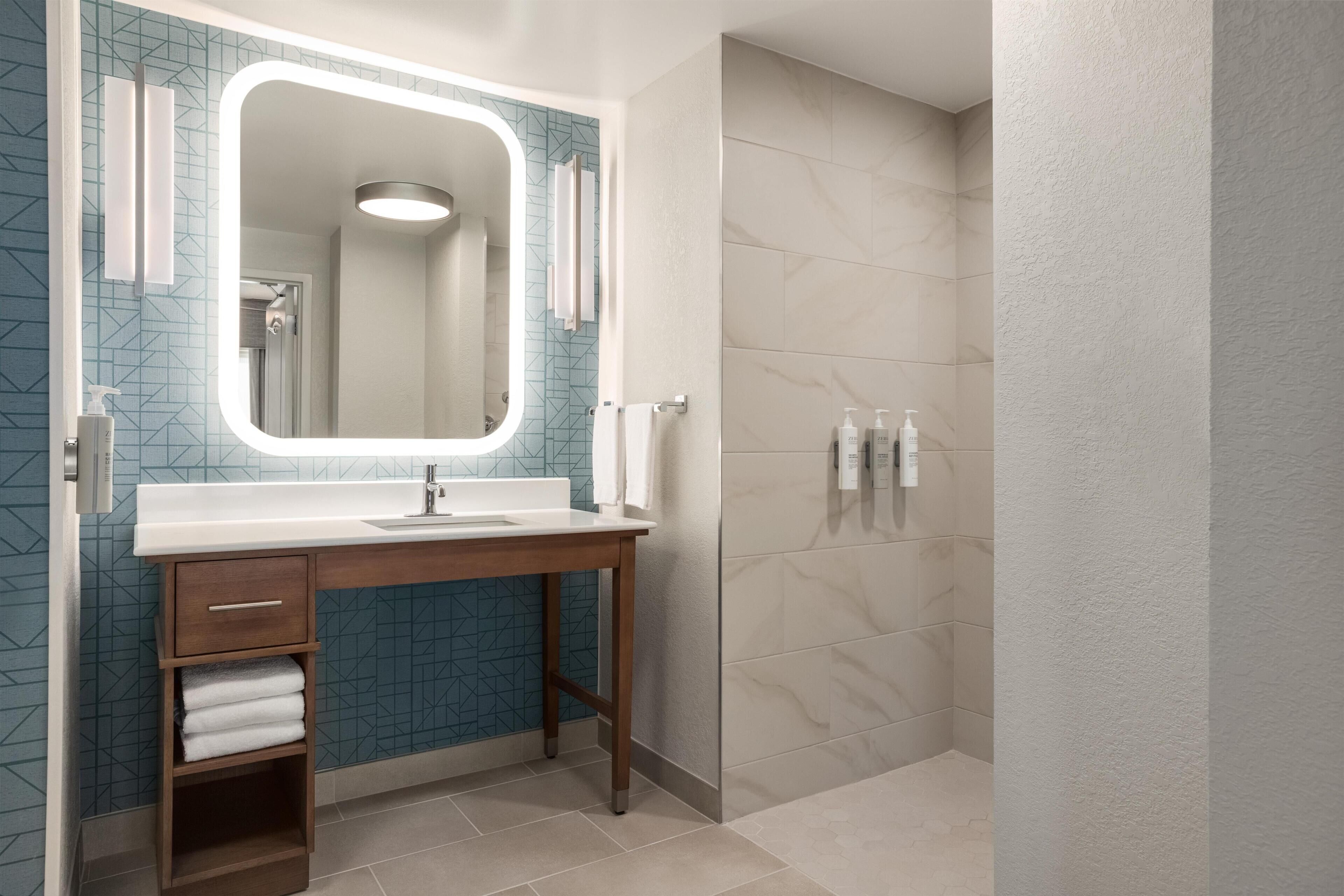 Baño con espejo, lavabo, toallero y zona de ducha.