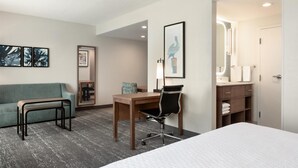 Una habitación de hotel con cama, escritorio, silla, sofá, espejo y obras de arte en las paredes.