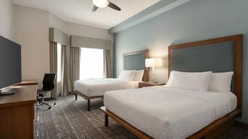 A hotel room with two beds, a desk, a chair, a ceiling fan, and a window with curtains.