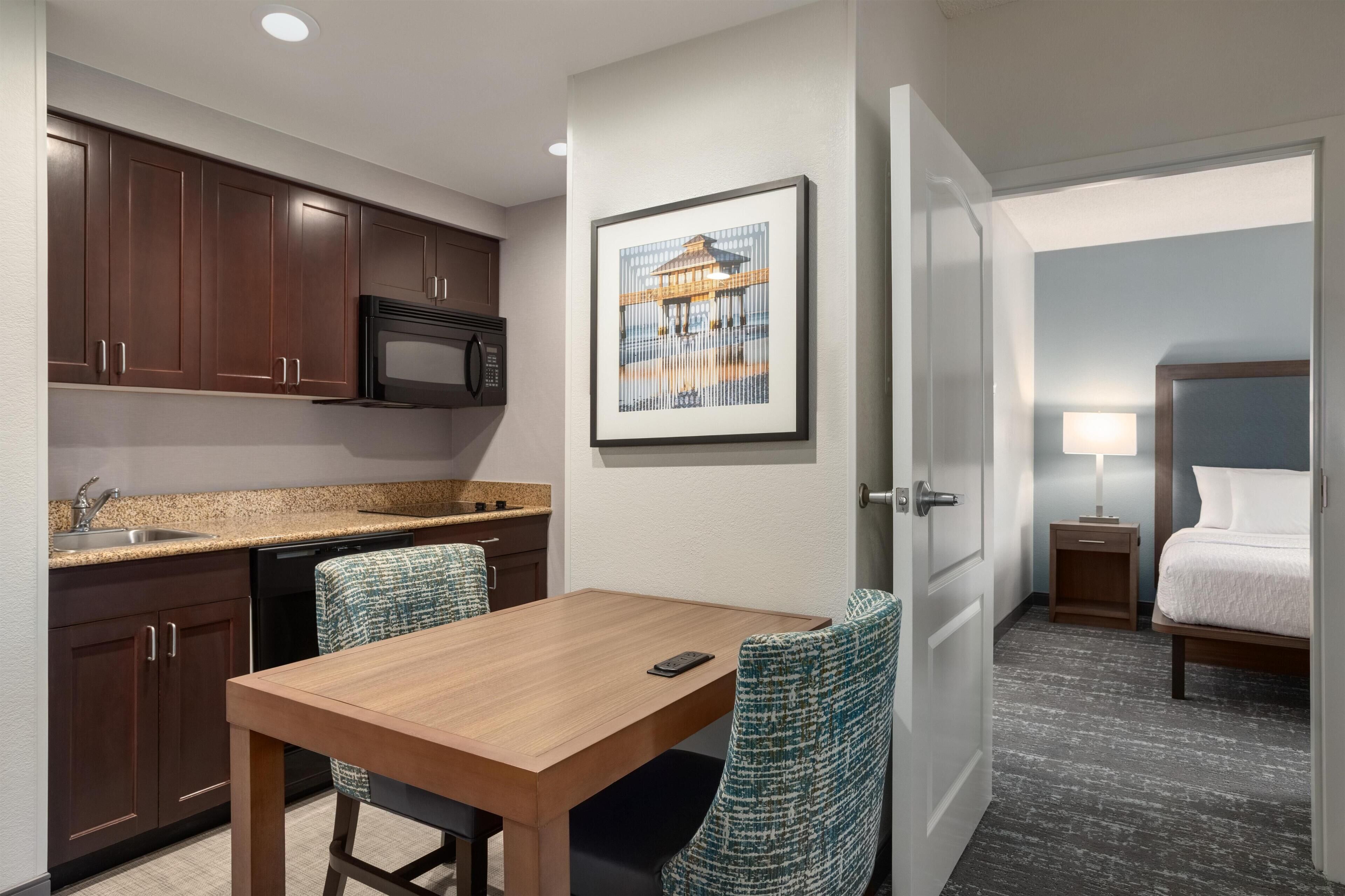 Une chambre d’hôtel compacte comprenant un coin cuisine, un espace repas, un lit et une petite table de chevet avec une lampe.