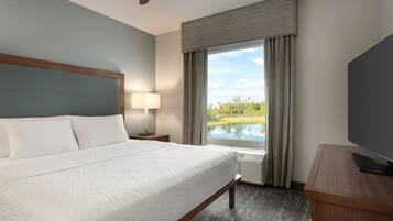 A hotel room with a bed, a desk, a television, a window with a view of a lake, and a ceiling fan.