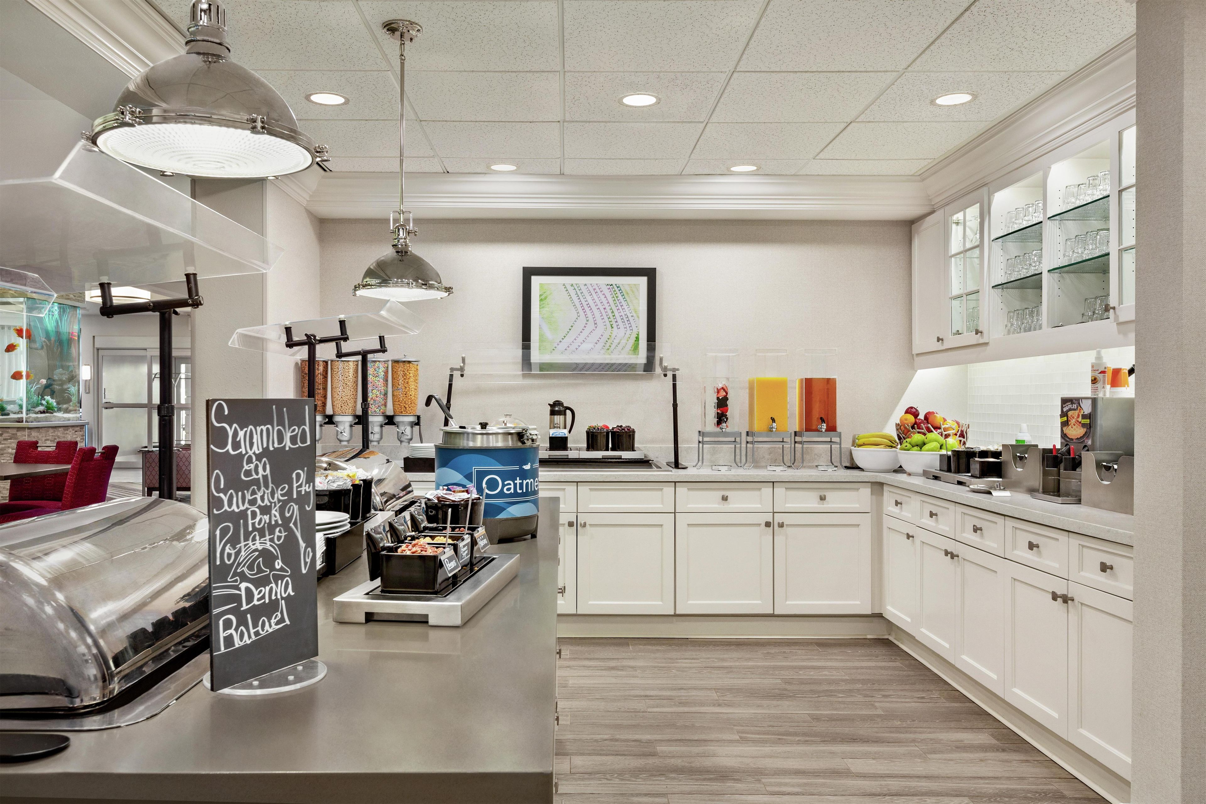 Una cocina moderna con armarios blancos, una encimera de acero inoxidable y diversos alimentos a la vista.