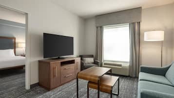 A hotel room with a bed, a TV, a desk, a sofa, and a window with curtains.