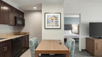 Habitación de hotel compacta con kitchenette, zona de comedor con dos sillas, cama, televisor y un cuadro en la pared.