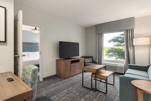 A hotel room with a bed, a TV, a desk, a chair, a sofa, and a window with curtains.