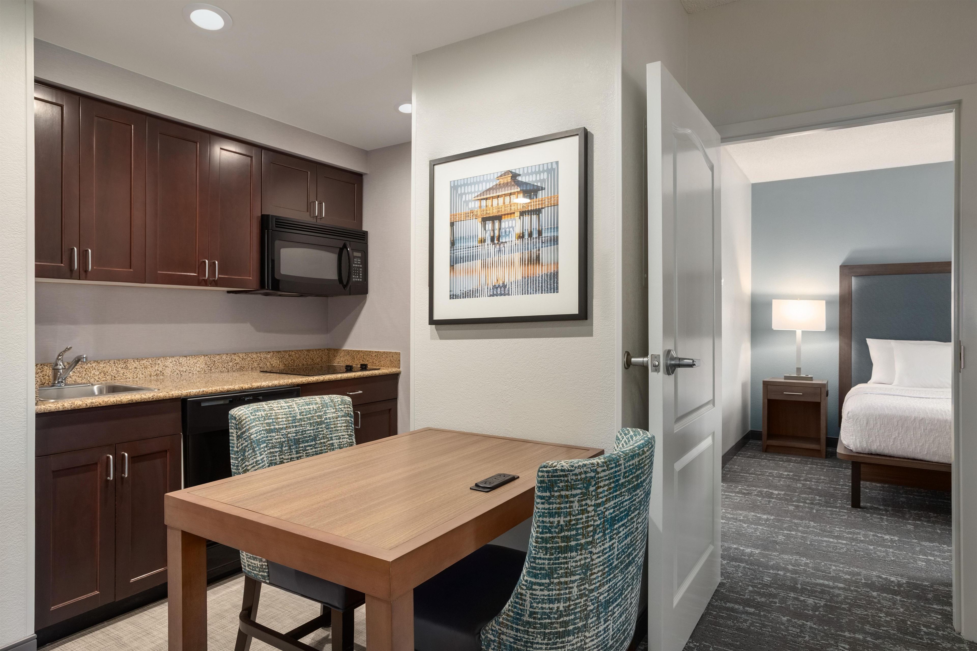 A hotel room with a kitchenette, a dining area, and a bed.
