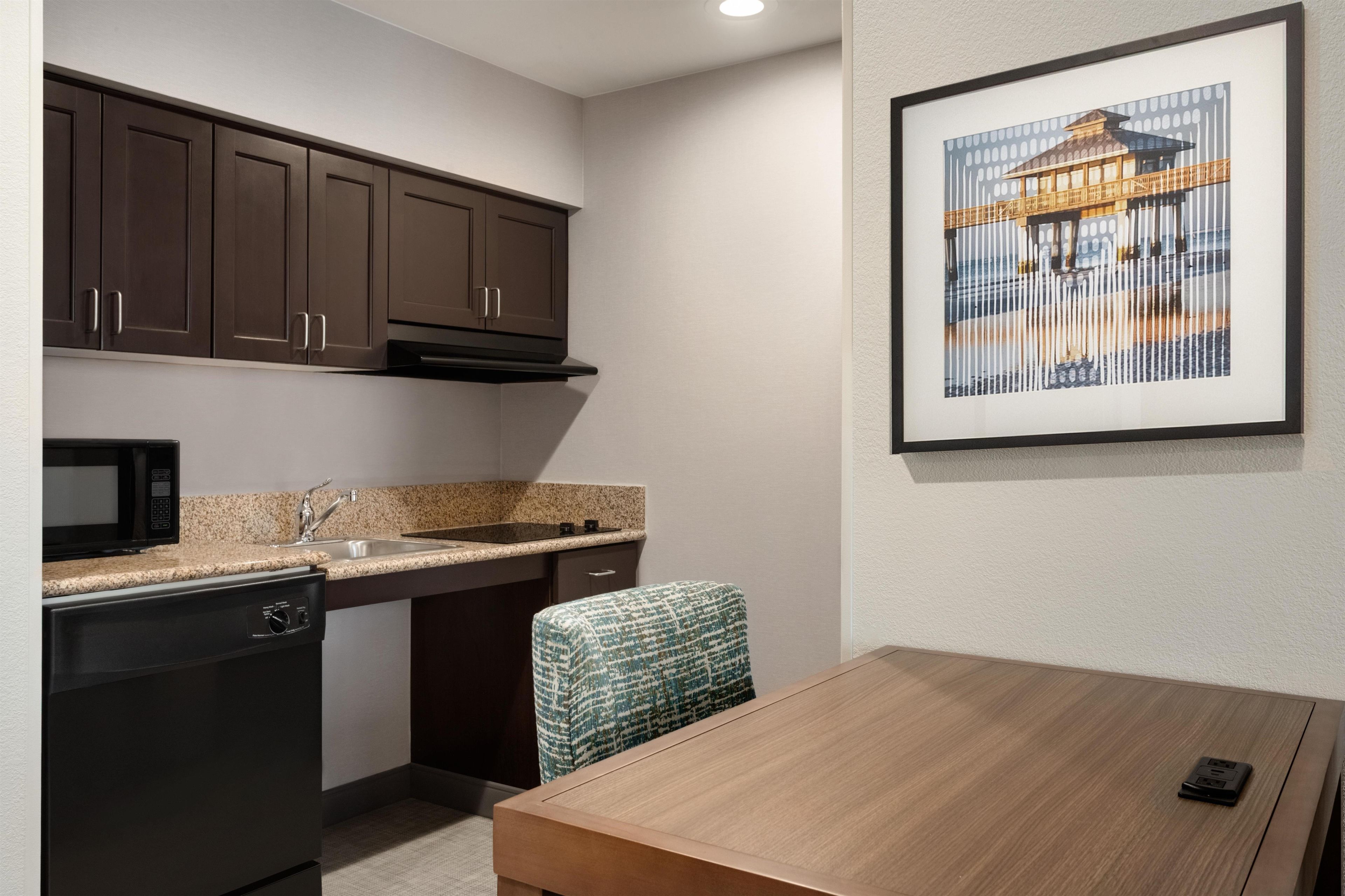 A compact kitchen with dark cabinets, a microwave, a sink, and a dining area with a table and chair.
