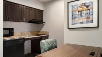 A compact kitchen with dark cabinets, a microwave, a sink, and a dining area with a table and chair.