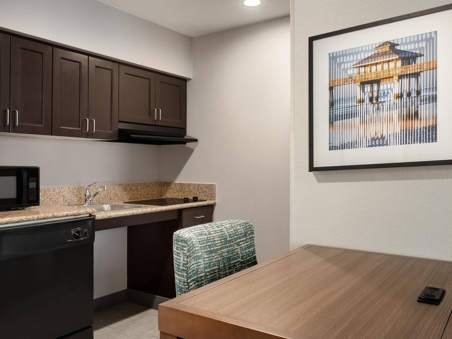 A compact kitchen with dark cabinets, a microwave, a sink, and a dining area with a table and chair.