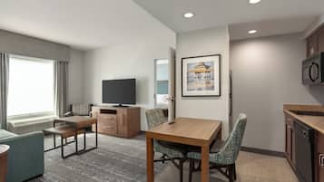A modern hotel room with a dining table, two chairs, a television, a framed picture, and a kitchen area.