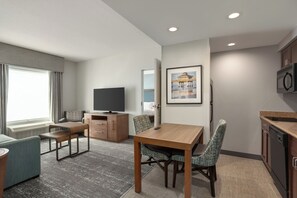 Habitación de hotel moderna con una mesa de comedor, dos sillas, un televisor, un cuadro enmarcado y una zona de cocina.