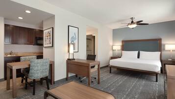 A hotel room with a bed, desk, chair, and kitchenette.