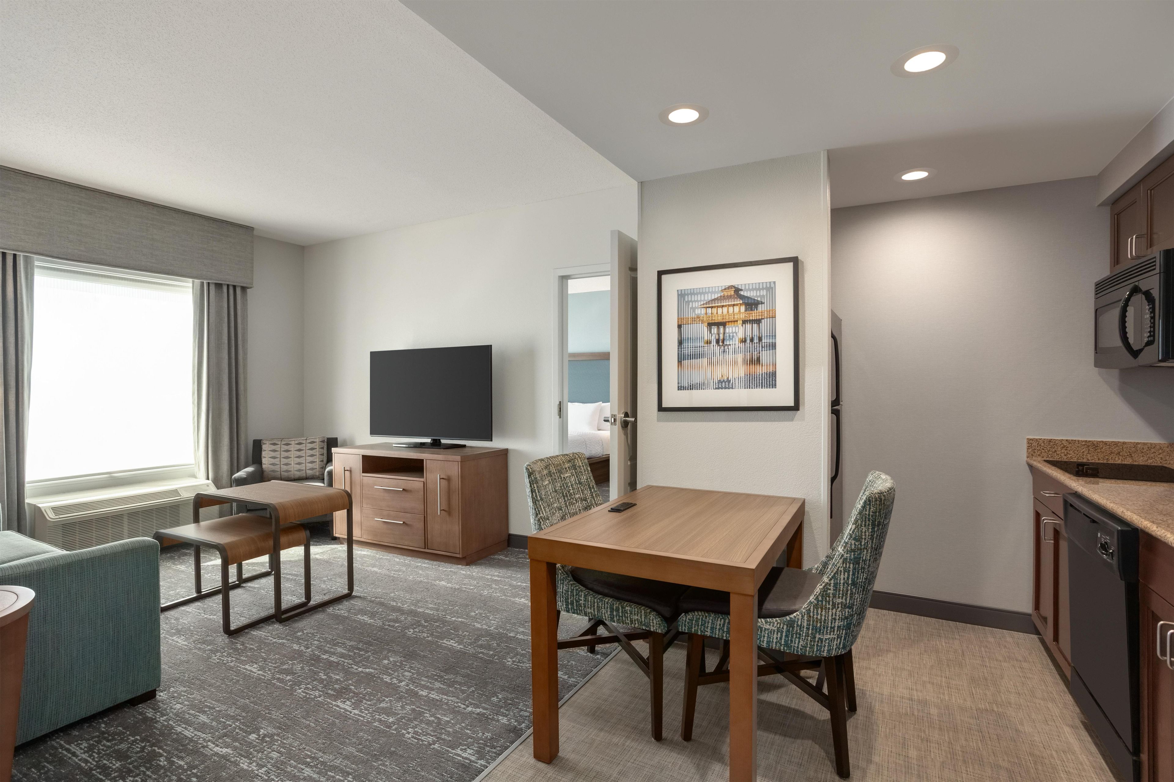 A hotel room with a dining table, chairs, a television, a microwave, and a kitchenette.