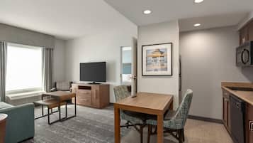 A hotel room with a dining table, chairs, a television, a microwave, and a kitchenette.