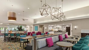 Un vestíbulo de hotel con zonas de estar, una cocina al fondo y un ventilador de techo.